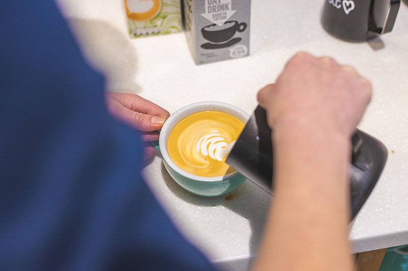 A person pouring milk for a barista coffee at Trebah Kitchen